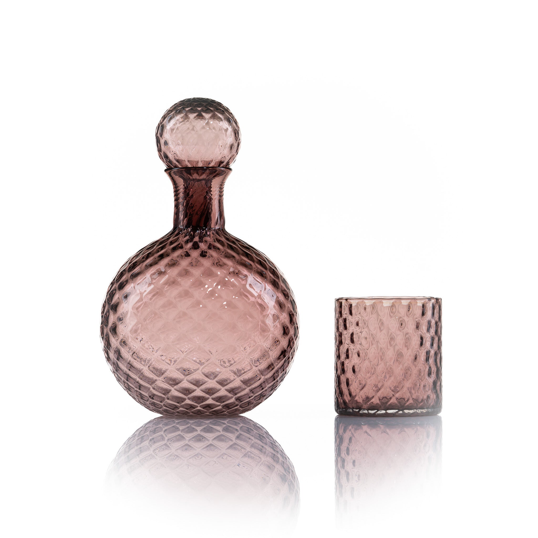 A modern and stylish clear glass barware set up, featuring a stack of cylindrical glass carafes and a small tumbler, arranged on a sleek, light surface. The composition is complemented by soft lighting in the background.