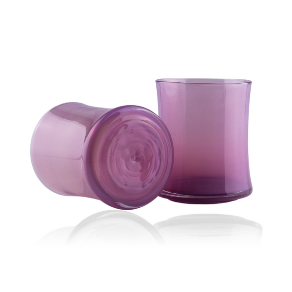 Displayed here are two rich lavender glass tumblers, one upended to showcase the circular base, and the other standing erect, exhibiting a sophisticated gradient of purple. The glassware casts a reflection on the surface below, emphasizing the depth of their elegant color and simple, stylish form.