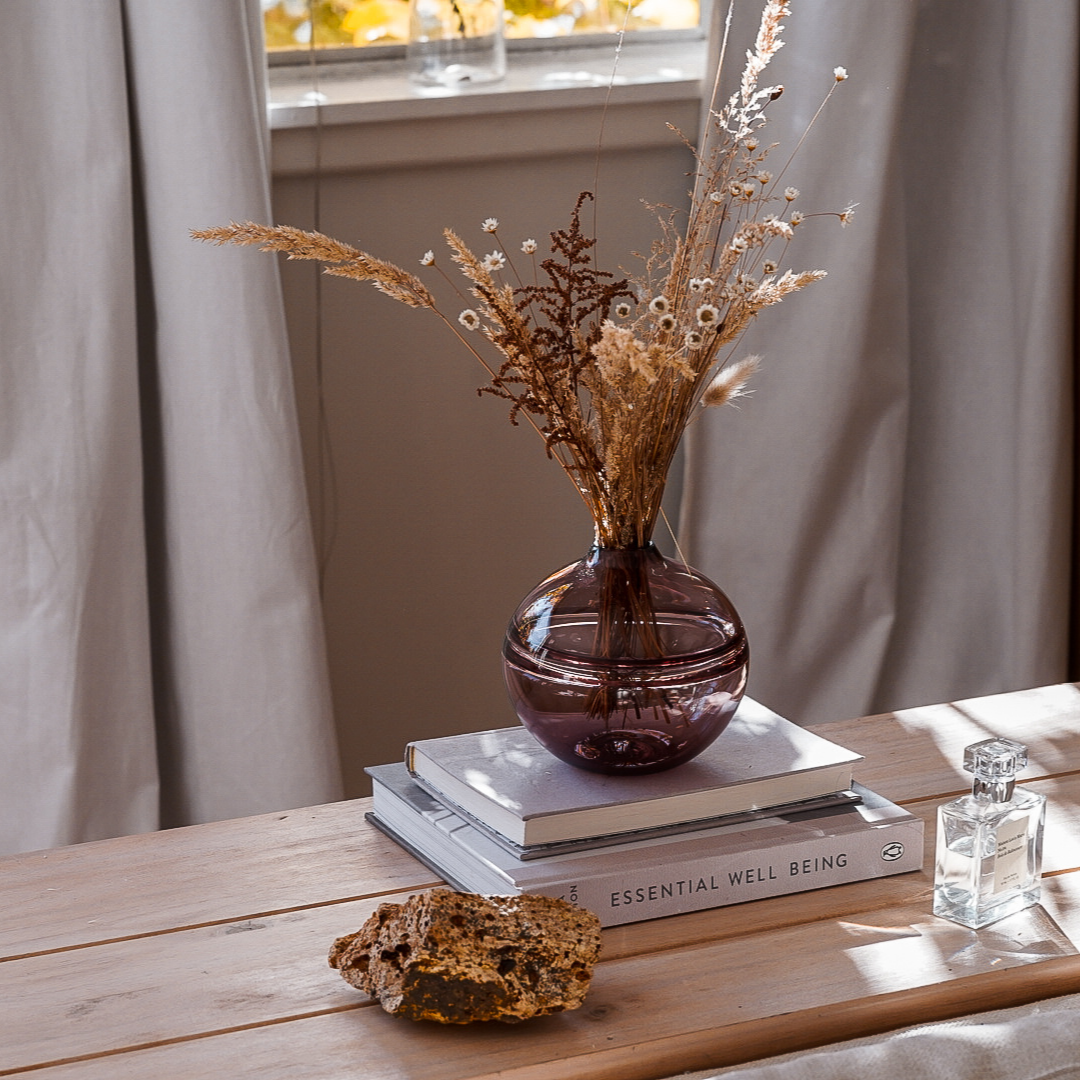 Round-bottomed halo glass vases in varying sizes, each with a small opening at the top, creating a harmonious arrangement of translucent, warm-toned spheres on a reflective surface