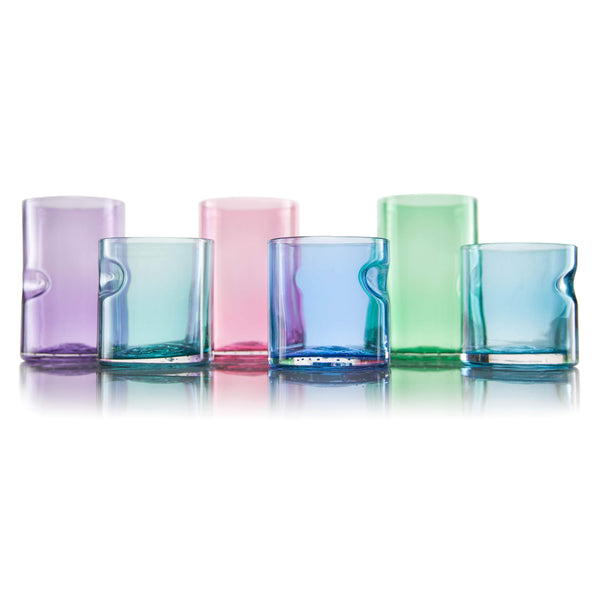 Vibrant glass tumblers of different heights stand side by side on a reflective surface. Their bright color and simple, elegant design with indentations for grip showcase the functional beauty of handcrafted glassware.