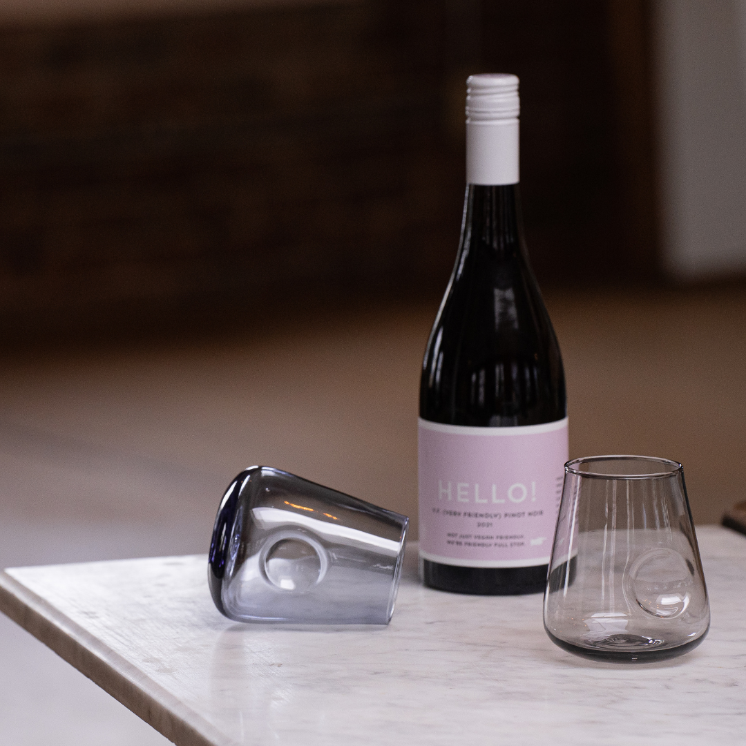 A stemless wine glass with a rounded base and distinctive thumb indent, showcased against a reflective surface with a black backdrop to enhance the glass's warm hues.