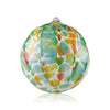 A glass Christmas orb featuring a vibrant collage of colors, reminiscent of a watercolor painting or oceanic scene, topped with a delicate glass loop for hanging, set against a white backdrop.