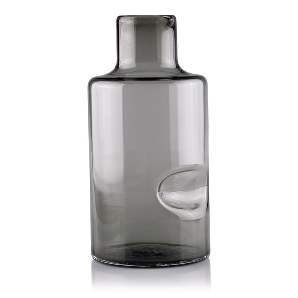 A sleek, smoky gray glass carafe with a modern design and a pronounced spout, positioned against a white background for a minimalist aesthetic.