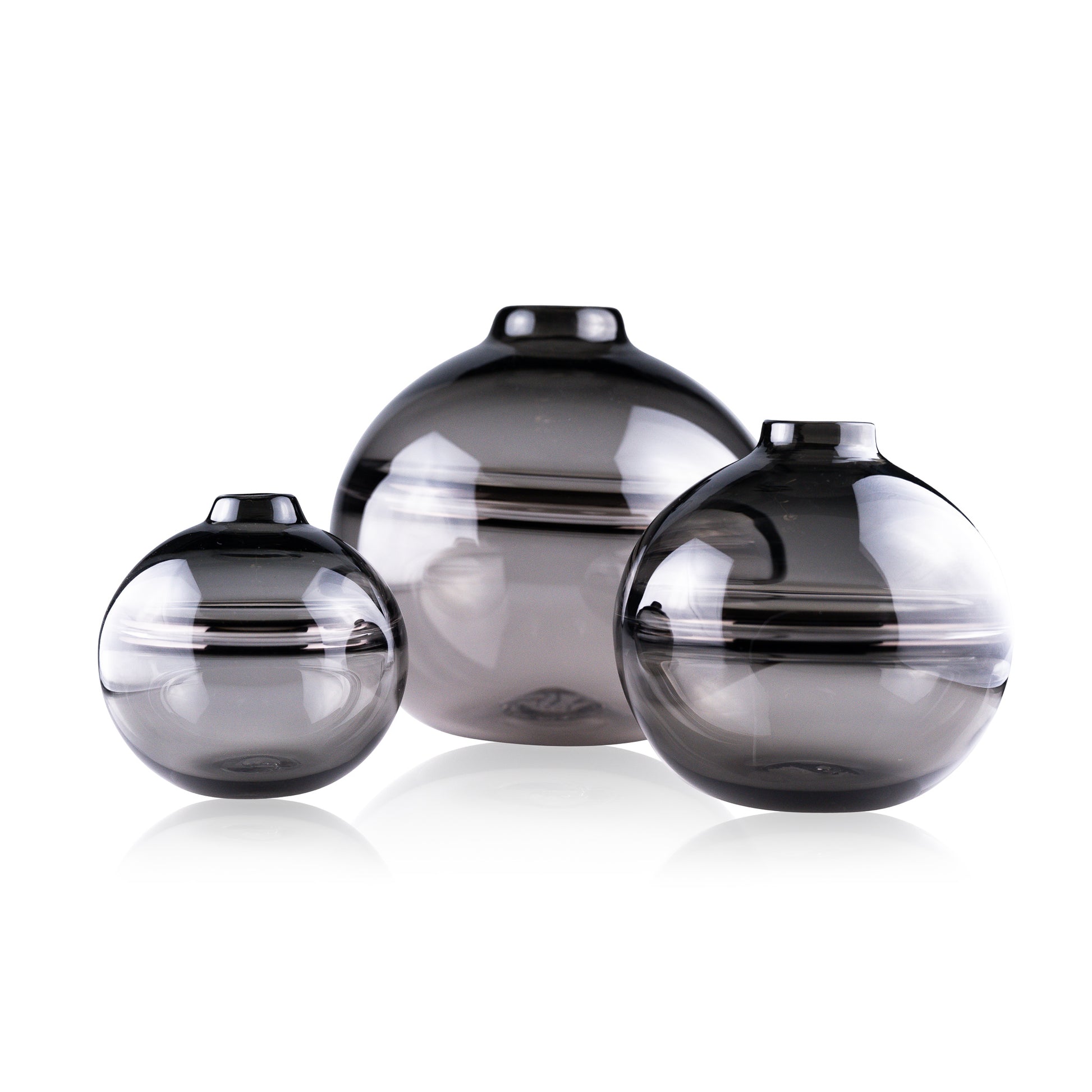 Round-bottomed halo glass vases in varying sizes, each with a small opening at the top, creating a harmonious arrangement of translucent, warm-toned spheres on a reflective surface