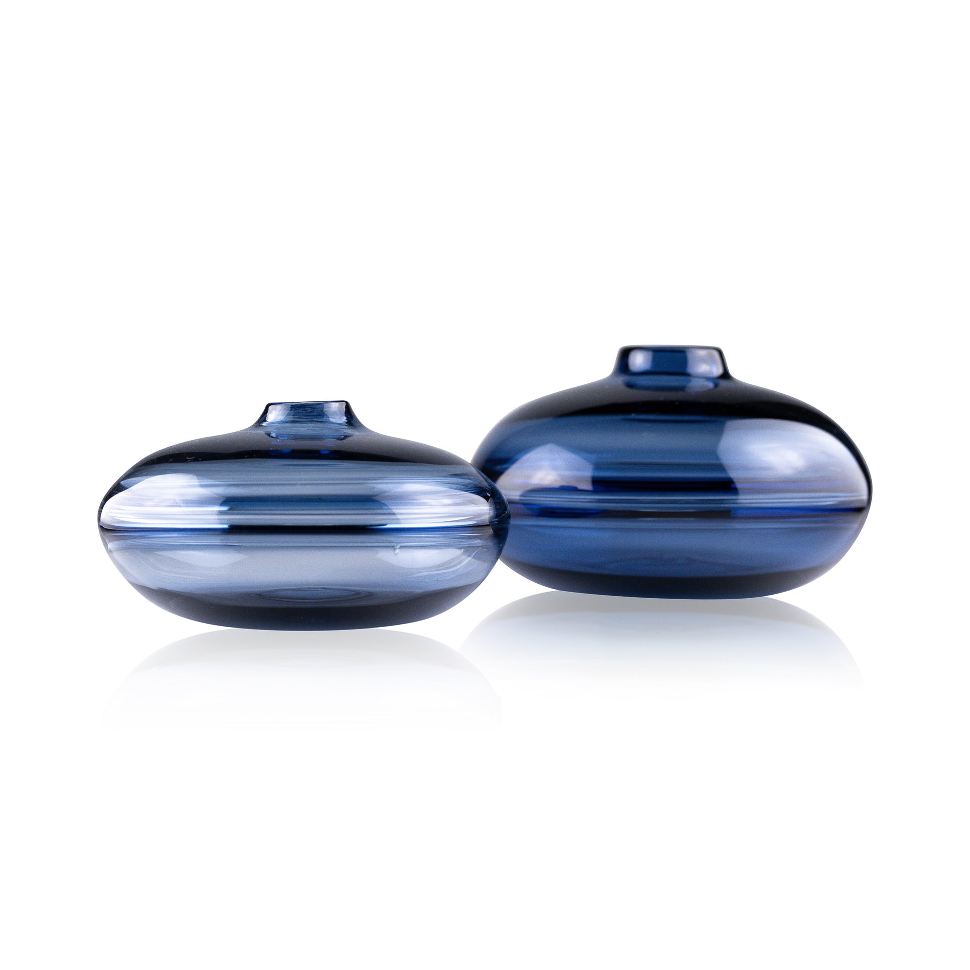 A squat glass vessel with a wide, flattened body and a narrow, raised lid, photographed against a white background, showcasing its smooth lines and tranquil, translucent color, reflective of serene, contemporary glass artistry.