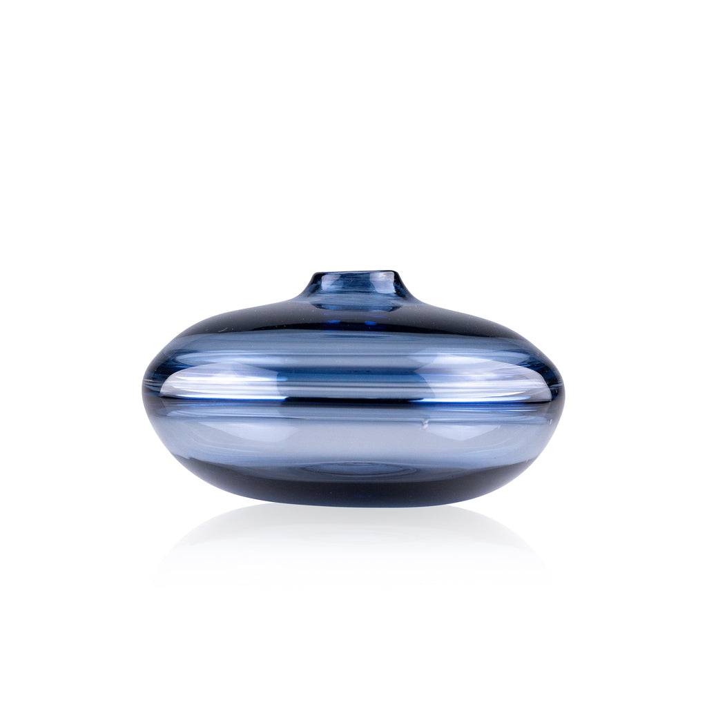 A squat glass vessel with a wide, flattened body and a narrow, raised lid, photographed against a white background, showcasing its smooth lines and tranquil, translucent color, reflective of serene, contemporary glass artistry.
