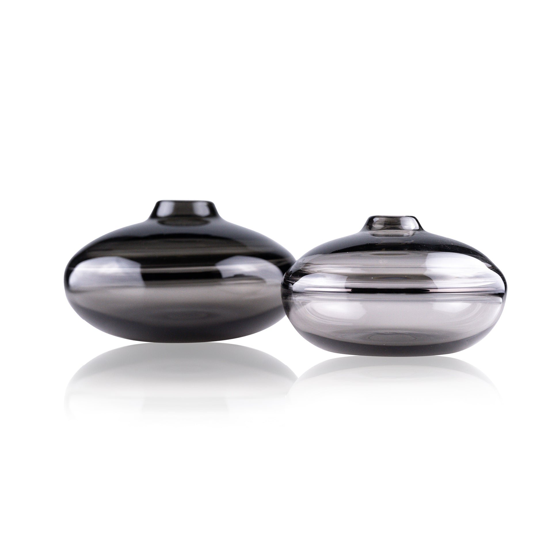 A squat glass vessel with a wide, flattened body and a narrow, raised lid, photographed against a white background, showcasing its smooth lines and tranquil, translucent color, reflective of serene, contemporary glass artistry.