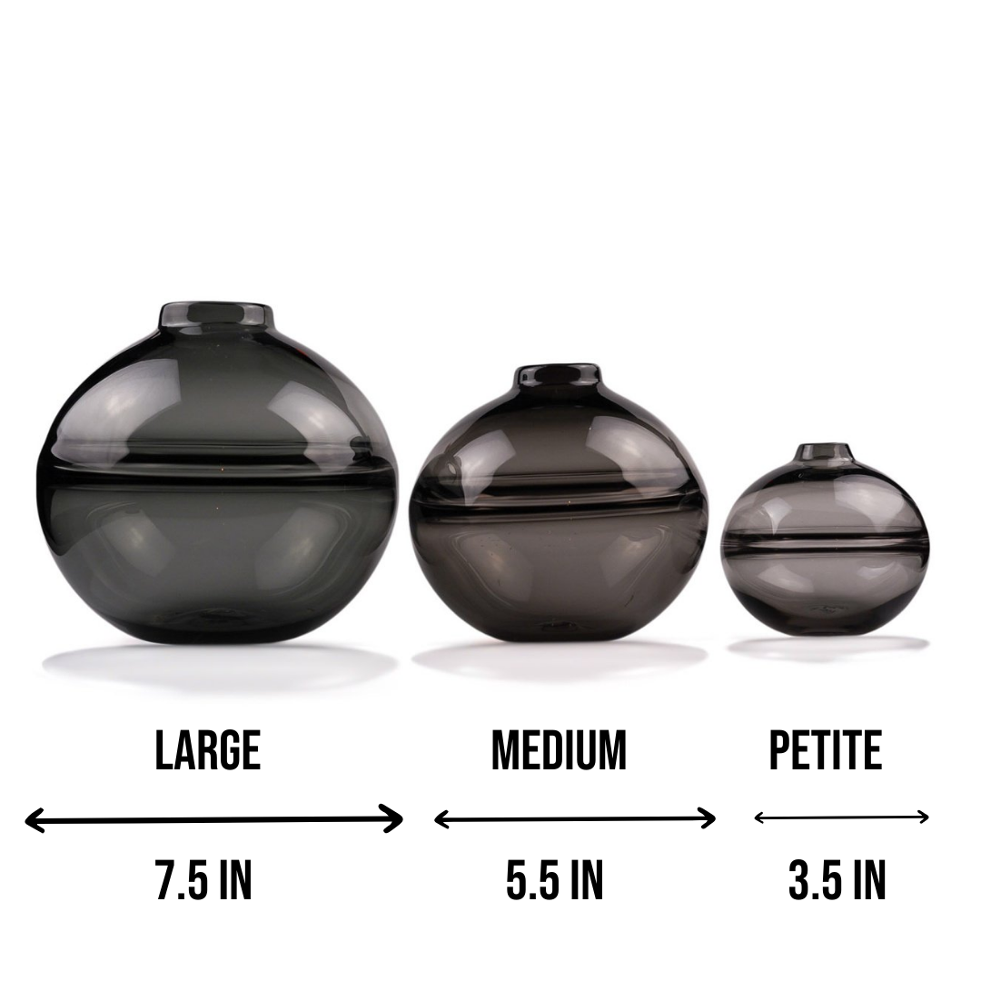 Round-bottomed halo glass vases in varying sizes, each with a small opening at the top, creating a harmonious arrangement of translucent, warm-toned spheres on a reflective surface