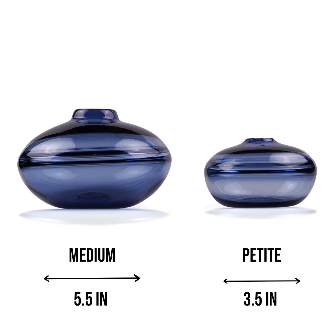 A squat glass vessel with a wide, flattened body and a narrow, raised lid, photographed against a white background, showcasing its smooth lines and tranquil, translucent color, reflective of serene, contemporary glass artistry.
