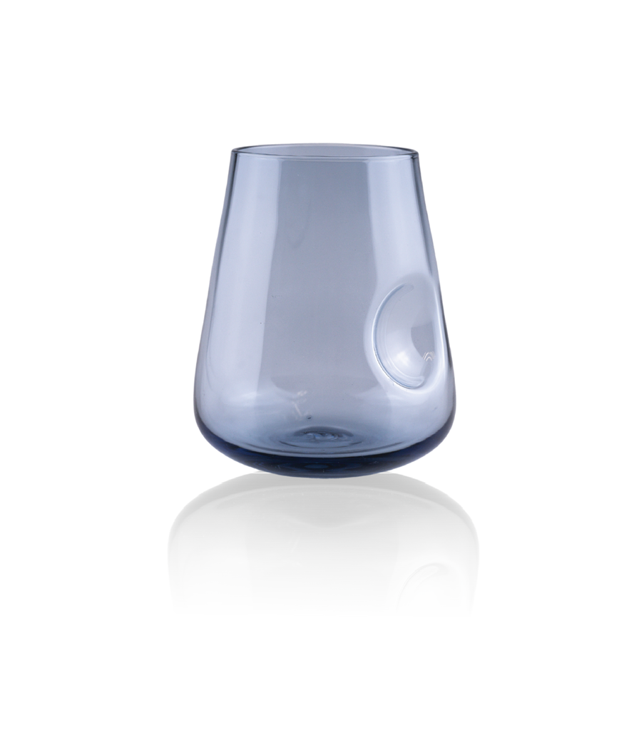 A stemless wine glass with a rounded base and distinctive thumb indent, showcased against a reflective surface with a black backdrop to enhance the glass's warm hues.