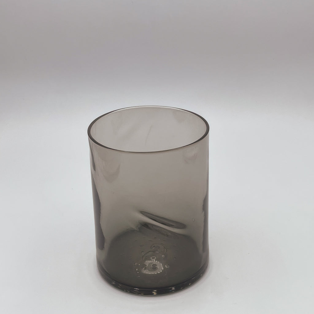 A sophisticated dark gray glass tumbler with a smooth thumb indent, embodying a modern and understated style, showcased against a clean white backdrop that emphasizes its elegant silhouette and transparent quality.