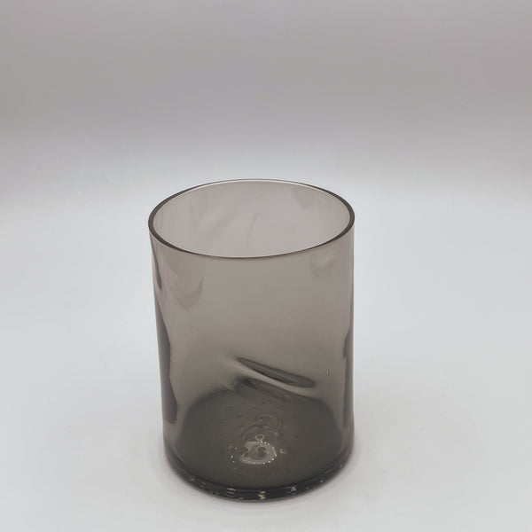 A sophisticated dark gray glass tumbler with a smooth thumb indent, embodying a modern and understated style, showcased against a clean white backdrop that emphasizes its elegant silhouette and transparent quality.