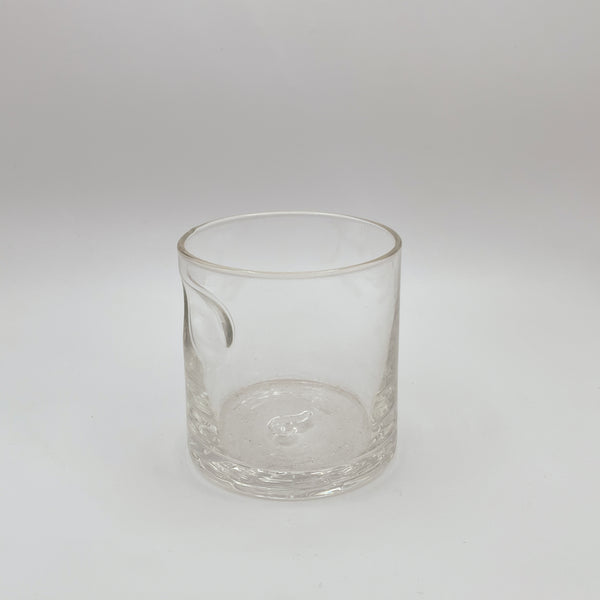 A clear glass tumbler with a stylish thumb indent, rimmed with a delicate gold band for an elegant touch. Its simple yet sophisticated design is emphasized by the pure white background, highlighting the glass’s crisp transparency.