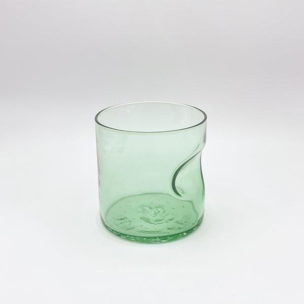 A light green glass tumbler with an ergonomic thumb indent, featuring a gentle gradient from a more vivid hue at the base to a subtle translucence. The tumbler's refreshing color and simple design are highlighted against the white background, evoking a sense of calm and cleanliness.
