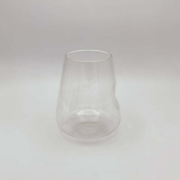 A clear glass stemless wine glass with a slightly tapered form and a thin gold rim, exuding a touch of elegance. It’s pictured against a white background, which highlights its simple yet refined design and transparent quality.
